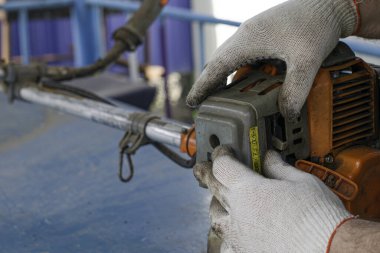 Çalışma eldivenlerinde usta, eski gaz budama makinesinin motorunu tamir eder karbüratör ve hava filtresinin kapağını açar.