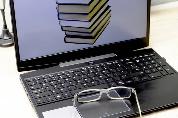 the concept of working at home on the Internet in teaching teaching study education reading glasses lying next to a laptop on the screen of which the image of a stack of books.