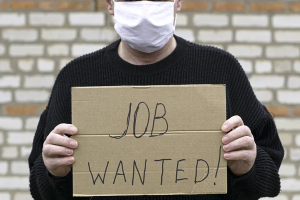 Concept unemployment and coronavirus a man in a medical hygienic mask is holding a cardboard tablet with a inscription job wanted — Stock Photo, Image