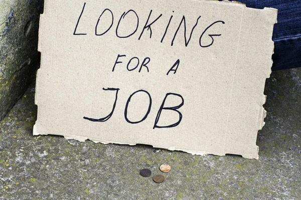 Kartonnen bord naast werklozen zittend op beton met op zoek naar een baan munten liggen in de buurt op een grond — Stockfoto