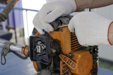 çalışan bir usta tornavidayla eski gaz budama makinesinin motorunu tamir eder yüksek voltajlı kablonun ucunu bujiden çıkarır