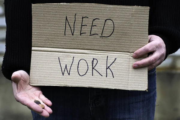 Der Arbeitslose hält in der einen Hand die Papptafel mit der Aufschrift Arbeitsbedürfnis in der anderen Hand die restlichen Münzen — Stockfoto