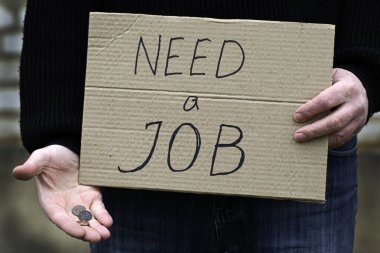 İşsiz kişi elinde bir karton tablet tutuyor. Üzerinde yazı var. Diğer elinde bir işe ihtiyacı var.