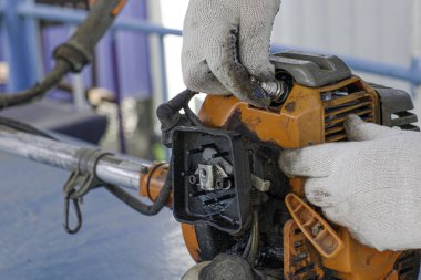 Eldiven ustası eski bir gaz kesicinin motorunu tamir eder, bujiyi söker.