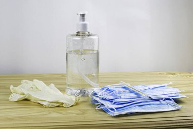 Masada tıbbi koruyucu maskeler, lastik eldivenler, termometre ve şeffaf bir şişede bir dezenfektan var.