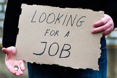 İşsiz kişi elinde bir karton tablet tutuyor. Üzerinde yazı var. Diğer elinde iş arıyor.