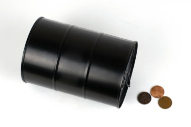 Düşen petrol fiyatları kavramı yanında duran siyah demir varil beyaz arka plana saçılmış küçük sikkelerdir.