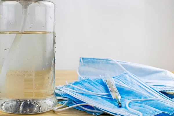 Sanitizer bottle, medical hygiene masks and thermometer lie on the table