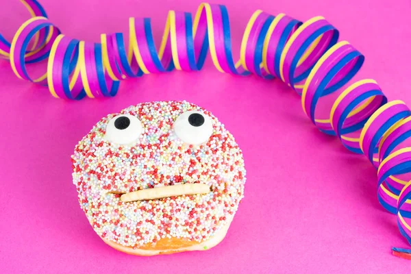 Delicious cake with a funny face, pink background and streamers