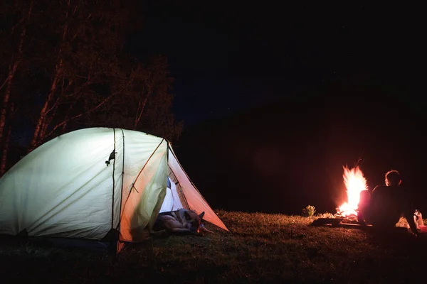 Des gens assis autour du feu de camp la nuit. Le chien dort près de la tente . — Photo