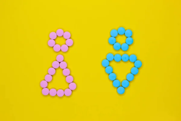 Чоловічі та жіночі символи з рожевих та синіх таблеток на жовтому тлі . — стокове фото