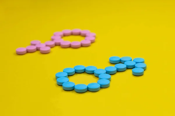 Pastillas azules en forma de signos de género de Marte y Venus sobre un fondo amarillo. Concepto médico . Imágenes De Stock Sin Royalties Gratis