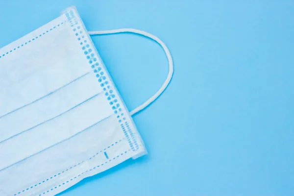 Medical mask with rubber ear straps close up with copy space on blue background. Coronavirus protection. COVID-19 proliferation prevention