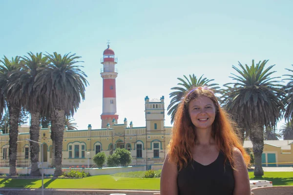 红头发快乐的白人白人女孩站在斯瓦科普蒙德 纳米比亚 的灯塔旁 双手放在臀部 愉快地微笑着 — 图库照片