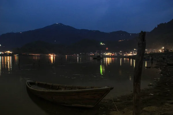 The calm and quiet Lake Feva at sunset is the main attraction of the city of Pokhara. Simple wooden fishing boats are tied to the shore.