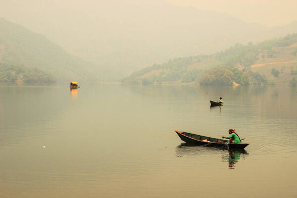 Pokhara, Nepal - March 12, 2014: The calm and quiet Lake Feva at sunset is the main attraction of the city of Pokhara. The nature of Nepal. Simple wooden fishing boats with fishermen sail on the lake.