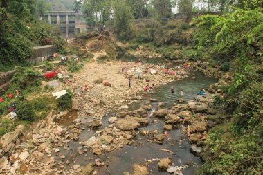 Pokhara, Nepal - 8 Nisan 2014: Nepal, Pokhara 'nın merkezindeki taşların arasında bir dağ nehrinde giysileri yıkayan ve yıkayan bir kalabalık.