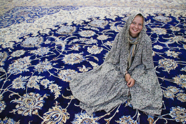A beautiful young girl sits in a richly decorated carpet.