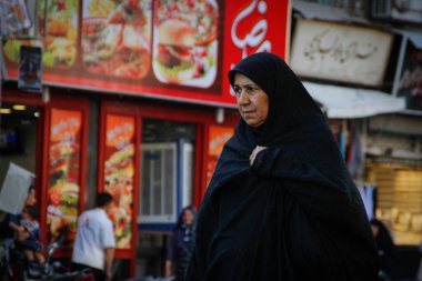 Şiraz, İran - 17 Mayıs 2017: Siyah peçeli yaşlı bir İranlı kadın dükkanlar arasında şehir caddesi boyunca ilerliyor..