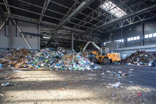excavator stacks trash in big pile at sorting modern waste recycling processing plant. Separate and sorting garbage collection. Recycling and storage of waste