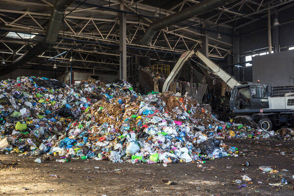 экскаватор складывает мусор в большую кучу при сортировке современных заводов по переработке отходов. Разделение и сортировка мусора. Переработка и хранение отходов
