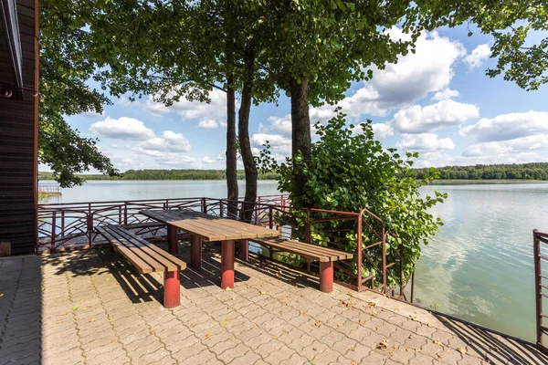 Stůl a lavice pro relaxaci u jezera v blízkosti dřevěné krajiny — Stock fotografie