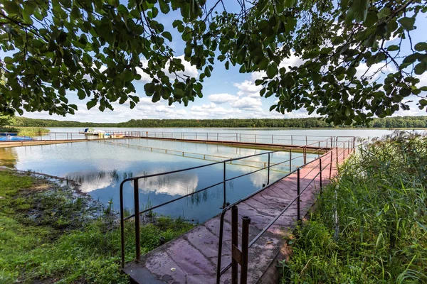 Muelle en la orilla de un gran lago en el día de verano con hermosas nubes. reflejo del cielo — Foto de Stock