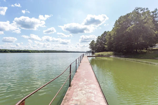 Muelle en la orilla de un gran lago en el día de verano con hermosas nubes. reflejo del cielo — Foto de Stock