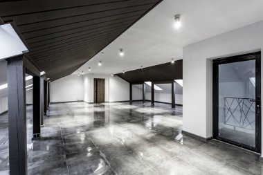 Ahşap sütunlar ve çatıdaki ıslak beton zemin ile döşenmemiş mobilyasız çatı katı. Siyah ve beyaz renkte.