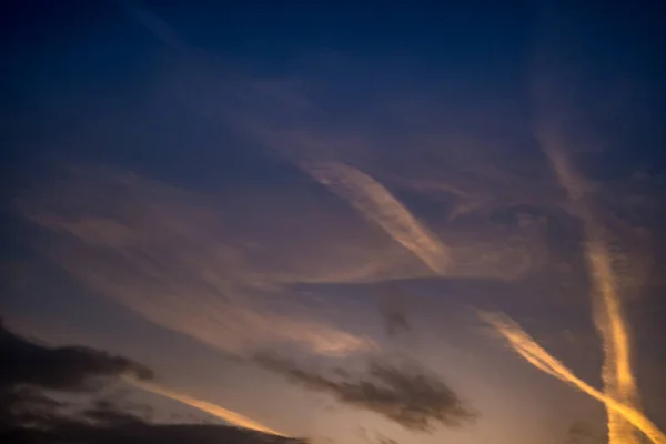 Verschwommener dunkler Himmelshintergrund mit abends flauschigen lockigen Wolken mit untergehender Sonne. gutes windiges Wetter — Stockfoto
