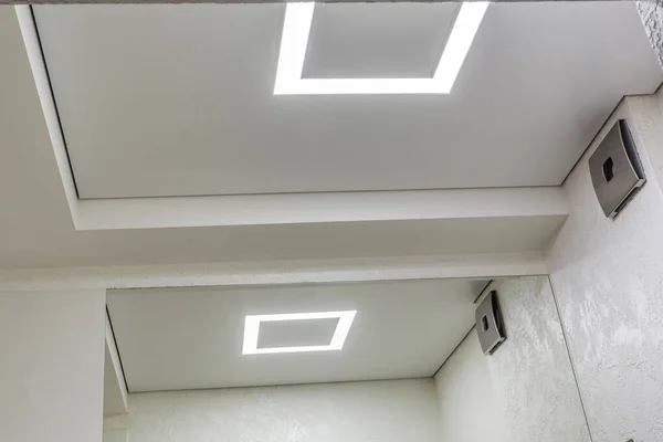 Галогенні плями світильників на підвісній стелі і гіпсокартоні в порожній кімнаті в квартирі або будинку. Натяжна стеля біла і складна форма . — стокове фото