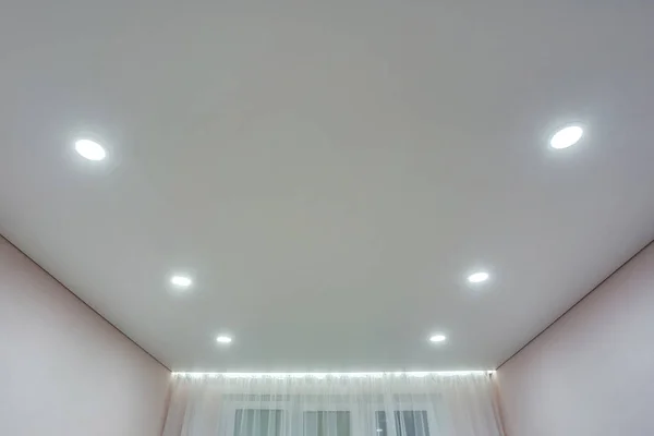 halogen spots lamps on suspended ceiling and drywall construction in in empty room in apartment or house. Stretch ceiling white and complex shape.