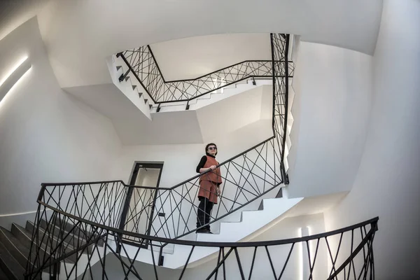 Mulher pequena em vidro preto permanece em um salão enorme com escadas de emergência e saída de evacuação. Ângulo largo — Fotografia de Stock