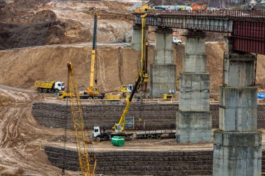 construction or reconstruction of highway concrete bridge over a wide river. construction machinery, trucks and cranes work
