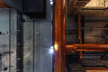 Halojen lekeli gri beton tavana bakmak ve çatı katındaki havalandırma ve turuncu havalandırma boruları olan lambalar.