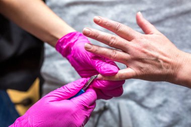 Manikür ustası pembe eldivenli. Manikür salonundaki eski cila kürkünü matkapla kazıyor. Kozmetoloji kliniğinde profesyonel manikür. Kuaförde ayaklar için hijyen. 