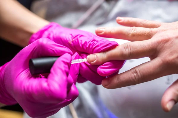 manicure master in pink gloves scraping off the old coat of varnish in manicure salon using drill.  Professional manicure in cosmetology clinic. Hygiene for feet in beauty salon.