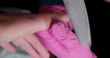 Pembe eldivenli manikür ustası mercimeği kullanarak manikür salonundaki tırnak ve şilinik tırnakları keser. Kozmetoloji kliniğinde profesyonel manikür. Güzellik salonunda eller için hijyen. 