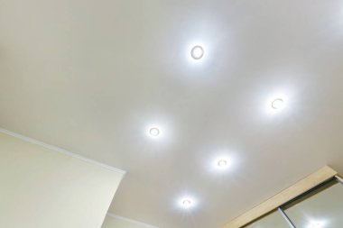 Halojen lambalı asma tavan ve boş bir oda ya da evde alçıpan inşaatı. Gergin tavan beyaz ve karmaşık şekil.