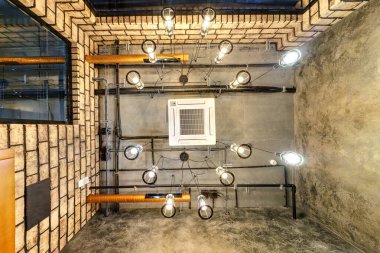Halojen lekeli gri beton tavana bakmak ve çatı katındaki havalandırma ve turuncu havalandırma boruları olan lambalar.