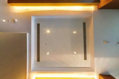 Halojen benekli lambalar ve alçıpan inşaatı ile asılı tavana bak. Daire ya da evdeki boş odada yangın alarmı sensörü var. Gergin tavan beyaz ve karmaşık şekil.