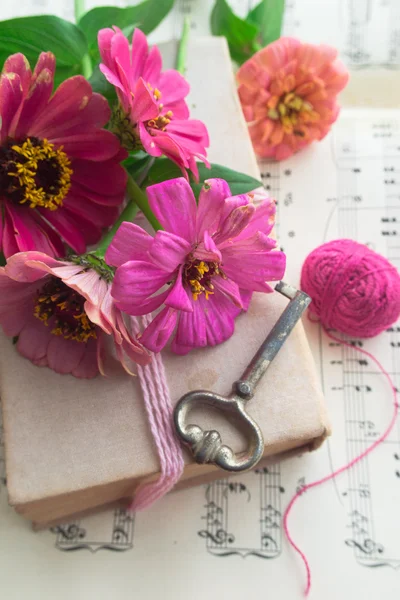 Old book with vintage key and pink flowers zinnia on music sheet background — Stock Photo, Image