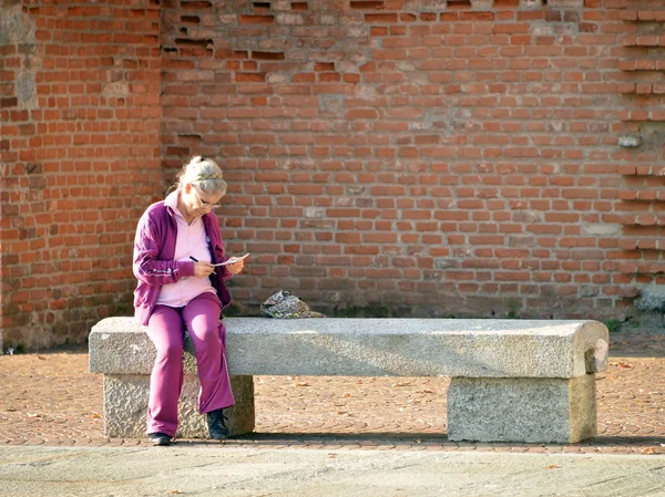 Una donna seduta su una panchina scrive su un taccuino — Zdjęcie stockowe