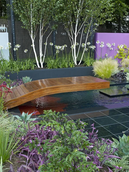 A colourful modern garden design with a range of flowers, plants and shrubs, decking, water and architectural features