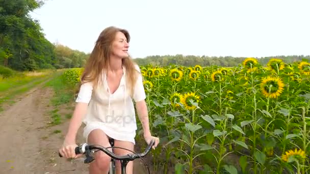 Mädchen fährt Fahrrad am Sonnenblumenfeld — Stockvideo