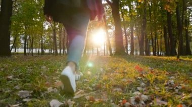 Bir kız elinde yapraklarla güzel bir parkta yürüyor. Sonbahar manzarası. Gün batımında parlak güneş ışınları. Kamera hareket halinde. Yavaş çekim