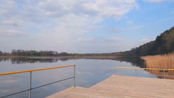 Piękne drewniane molo nad jeziorem. Słoneczny dzień z błękitnym niebem i białymi chmurami. Kamera porusza się do przodu. Zwolniony ruch — Wideo stockowe