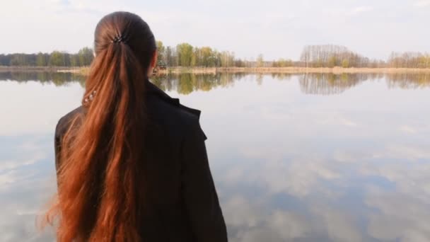 한 외로운 소녀는 호수 근처에 있는 나무로 된 부두에 서 있다. 화창 한 날씨입니다. 밝은 푸른 하늘. 카메라 가작 동중이다. 느린 동작 — 비디오