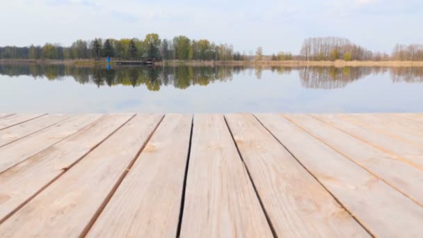 Muelle de madera cerca del pintoresco lago. Hermosa casa solitaria en el otro lado. Cielo azul brillante. Reflejo de nubes en el agua. La cámara avanza. Movimiento lento — Vídeos de Stock