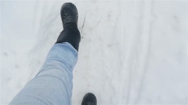 Siyah çizmeli bir adam beyaz karda yürüyor. Bacakları yakın çekim. Yavaş çekim